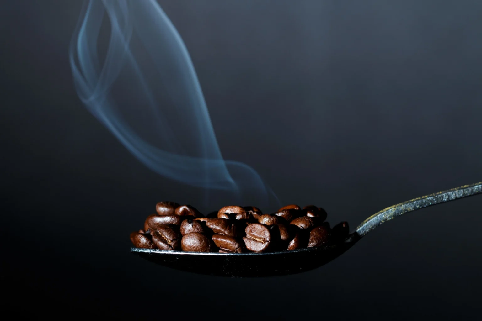 une cuillère vue de côté contenant des grains de cafés fumant
