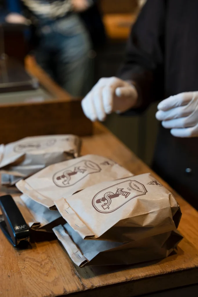 des sachets de café en train d'être pesé sur une balance par des mains portant des gants en plastique blanc